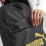 Close-up of a black backpack being opened, a hand gripping the zipper, with a yellow Puma logo visible on the lower front.