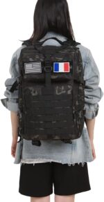 Back view of a person wearing a black camouflage tactical backpack with US and French flag patches over a denim jacket.