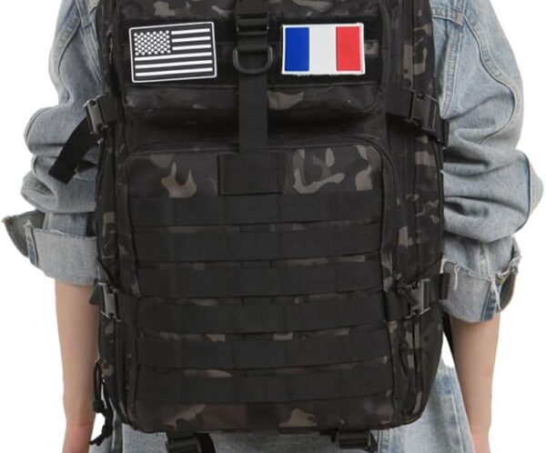 Back view of a person wearing a black camouflage tactical backpack with US and French flag patches over a denim jacket.