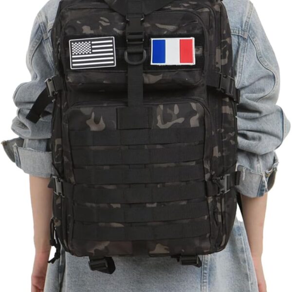 Back view of a person wearing a black camouflage tactical backpack with US and French flag patches over a denim jacket.