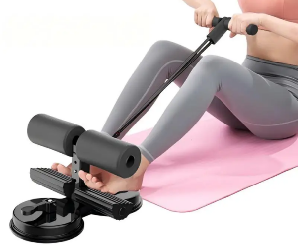 Compact pedal exerciser with foam rollers and suction base, being used on a pink exercise mat for leg/arm workouts.
