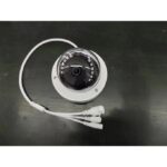 White dome security camera with a circular lens and attached white power/video cables on a dark work surface.