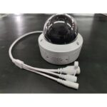 Dome security camera with three white cables coiled on a dark work surface.