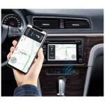 Person holding a smartphone with a map app, pointing to navigation while car interior shows a built‑in GPS screen and wireless data icon on the center console.