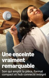 Woman relaxing on a sofa next to a round smart speaker on a wooden table; ad text mentions a remarkable compact connected speaker.