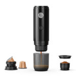 Disassembled black coffee capsule device with lid and several capsules separated, showing internal parts and ground coffee cups lined up below